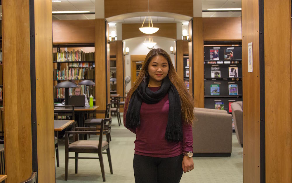 female students stands in the library in between columns of books and magazines