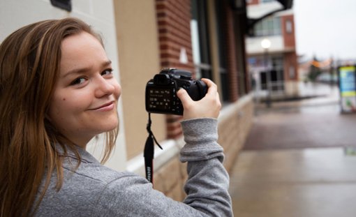 Kailey looks over her shoulder, smiling while holding a camera to take photos on Rowan Boulevard