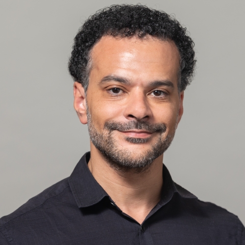 Jamal Jones wearing a black shirt, beard and mustache, smiling at the camera.