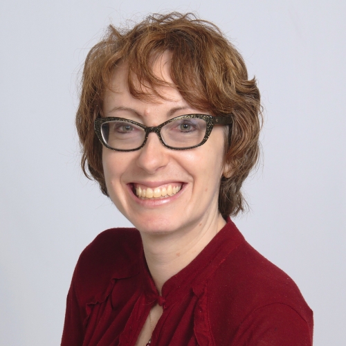 Jennifer Schaupp wearing a red shirt and black glasses, smiling at the camera