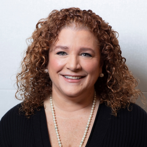 Lorna Boucher wearing a black shirt with a pearl necklace smiling at the camera.