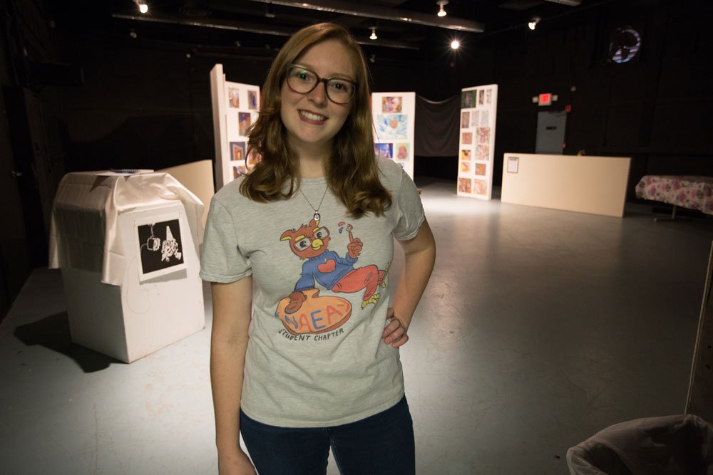 female student stands with hand on hip with art gallery exhibit behind her at 301 High Street Gallery